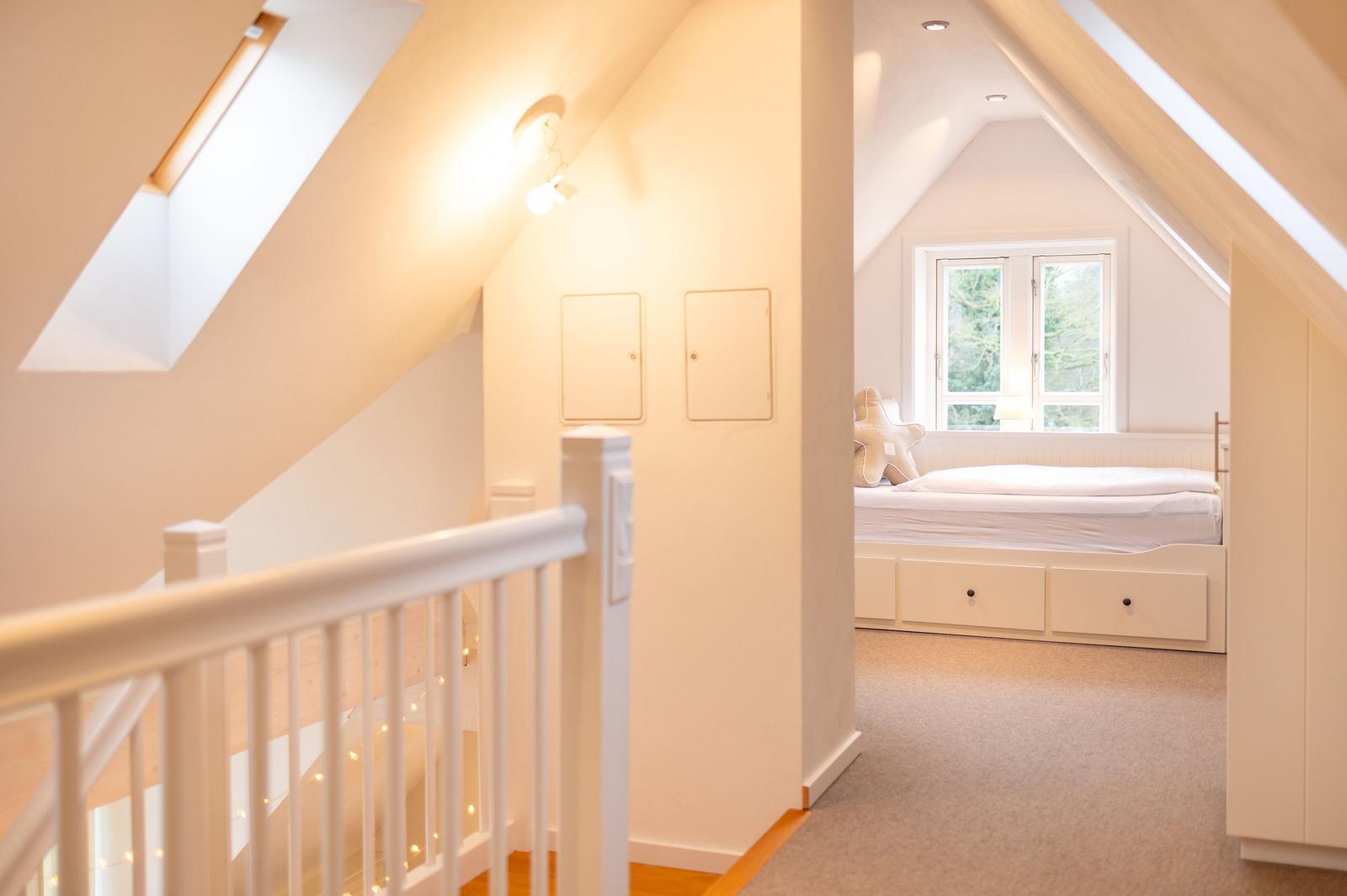 Dachgeschosszimmer mit Bett und Fenster. Blick von der Treppe.