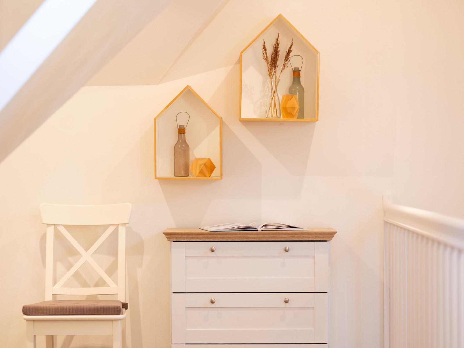 Weißer Schrank mit Holzoberfläche, daneben Stuhl und Wandregale mit Dekoration.