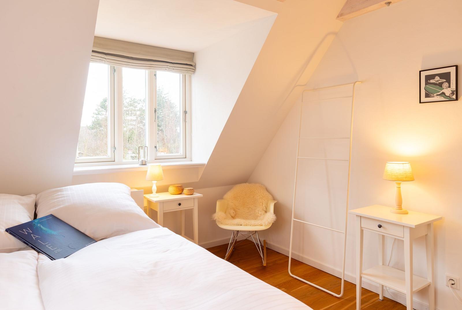 Schlafzimmer mit Dachschräge, Bett, Nachttisch, Stuhl und Fenster.