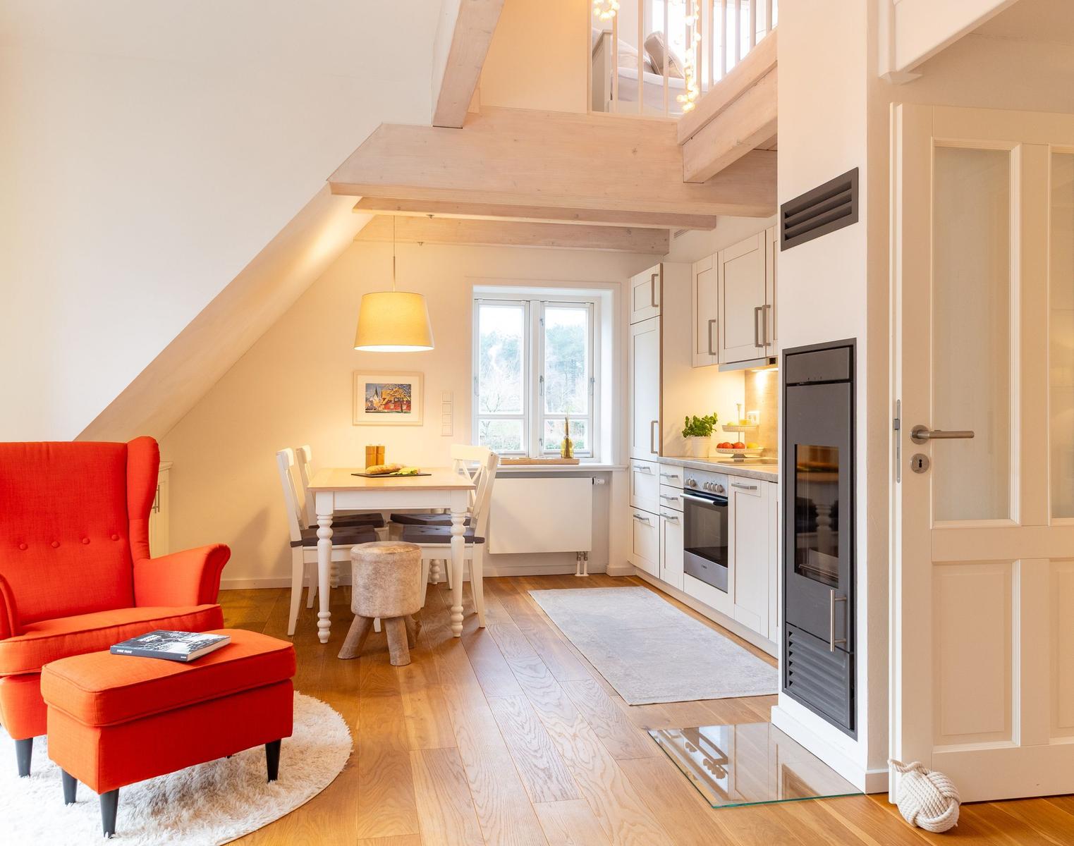 Wohnküche mit Essbereich, rotem Sessel und Dachbodenbereich.