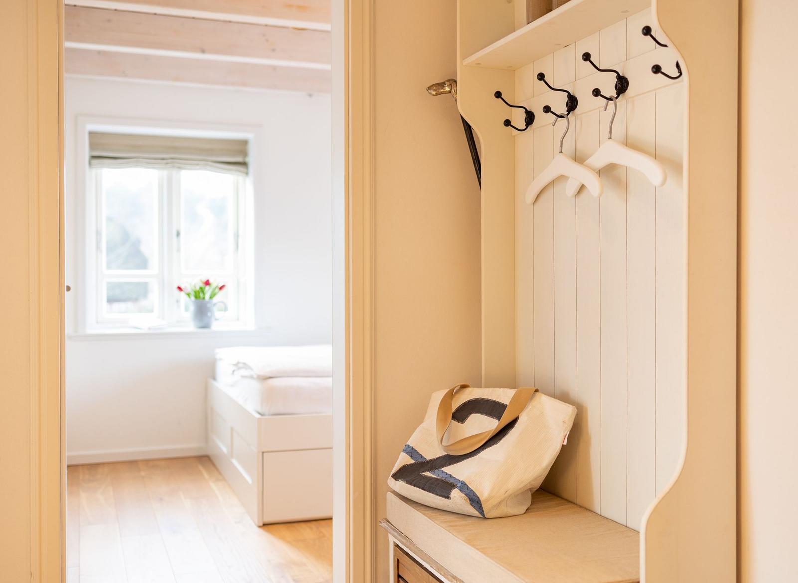 Ein Flur mit Garderobe und Blick in ein Schlafzimmer mit Fenster und Bett.