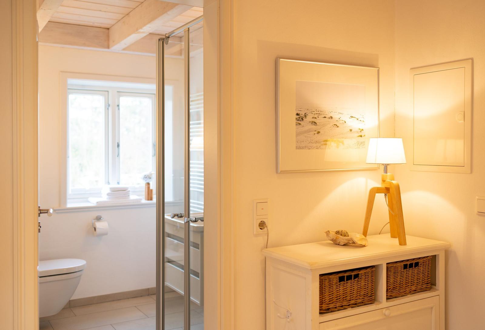 Badezimmer mit Dusche und Toilette. Nebenraum mit Schrank, Lampe und Bild.
