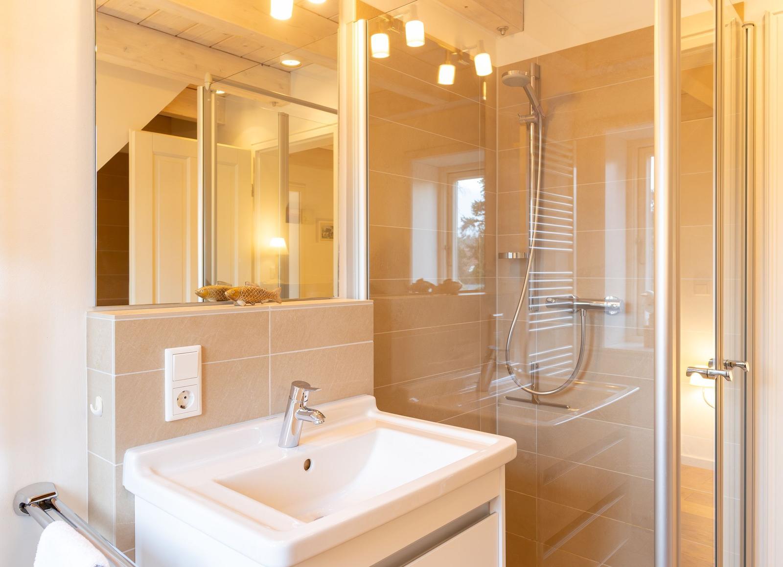 Bad mit Dusche, Waschbecken und Spiegel. Zwei Fische dekorieren den Spiegelrand.