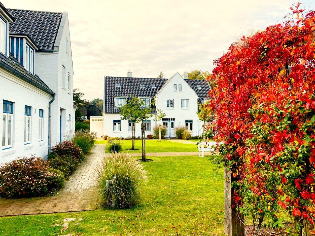 Weißes Haus mit Garten und rotem Busch im Vordergrund.
