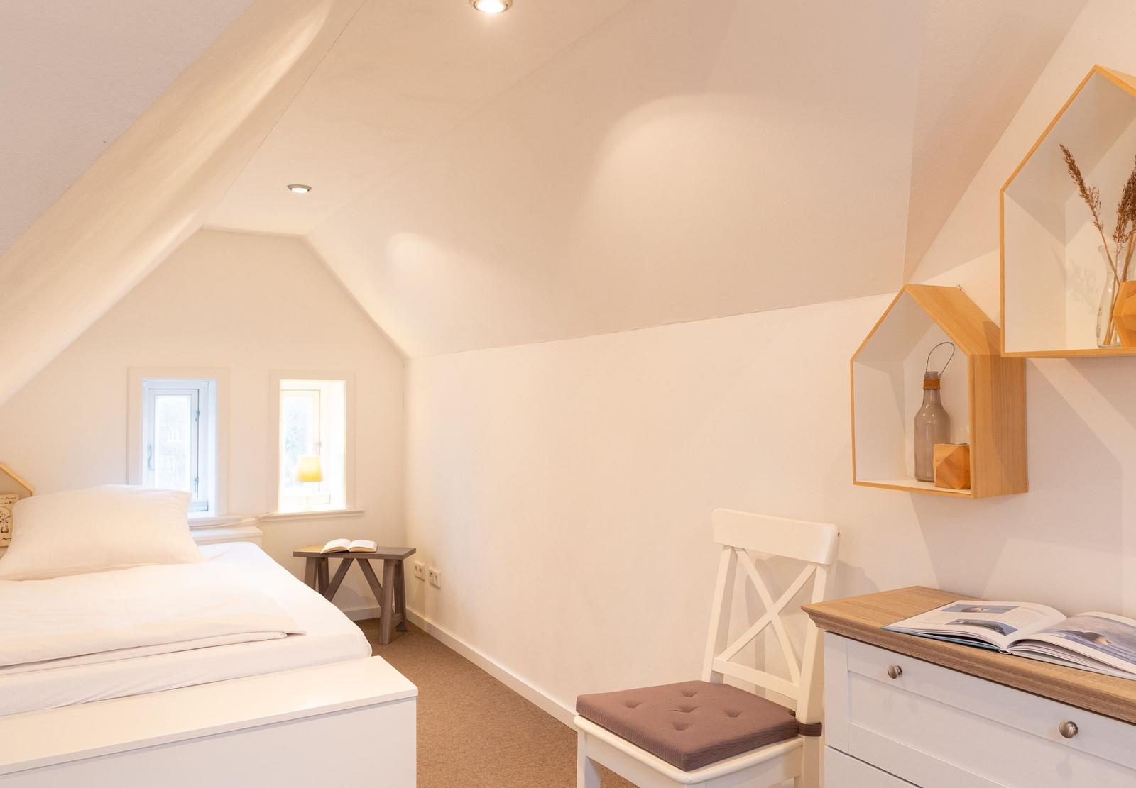 Schlafzimmer mit Dachschrägen, Bett, Stuhl und Schreibtisch.