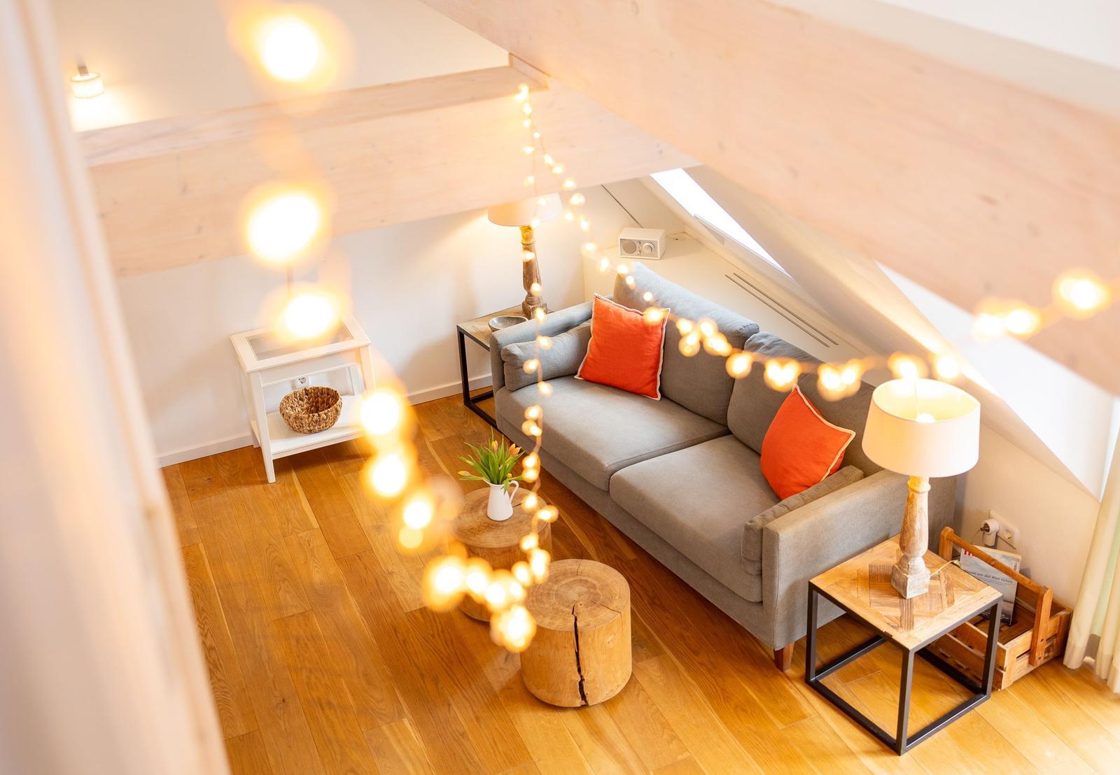 Wohnzimmer mit Sofa, Tischen und Lichterkette unter Holzdecke.