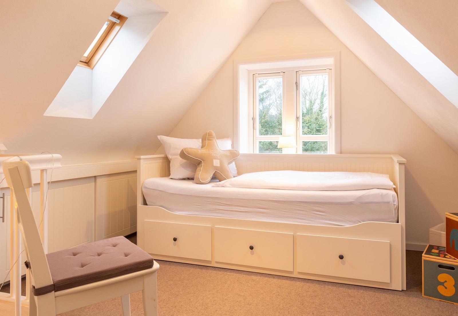 Ein Schlafzimmer mit Dachschräge, Fenster, Bett und Stuhl.