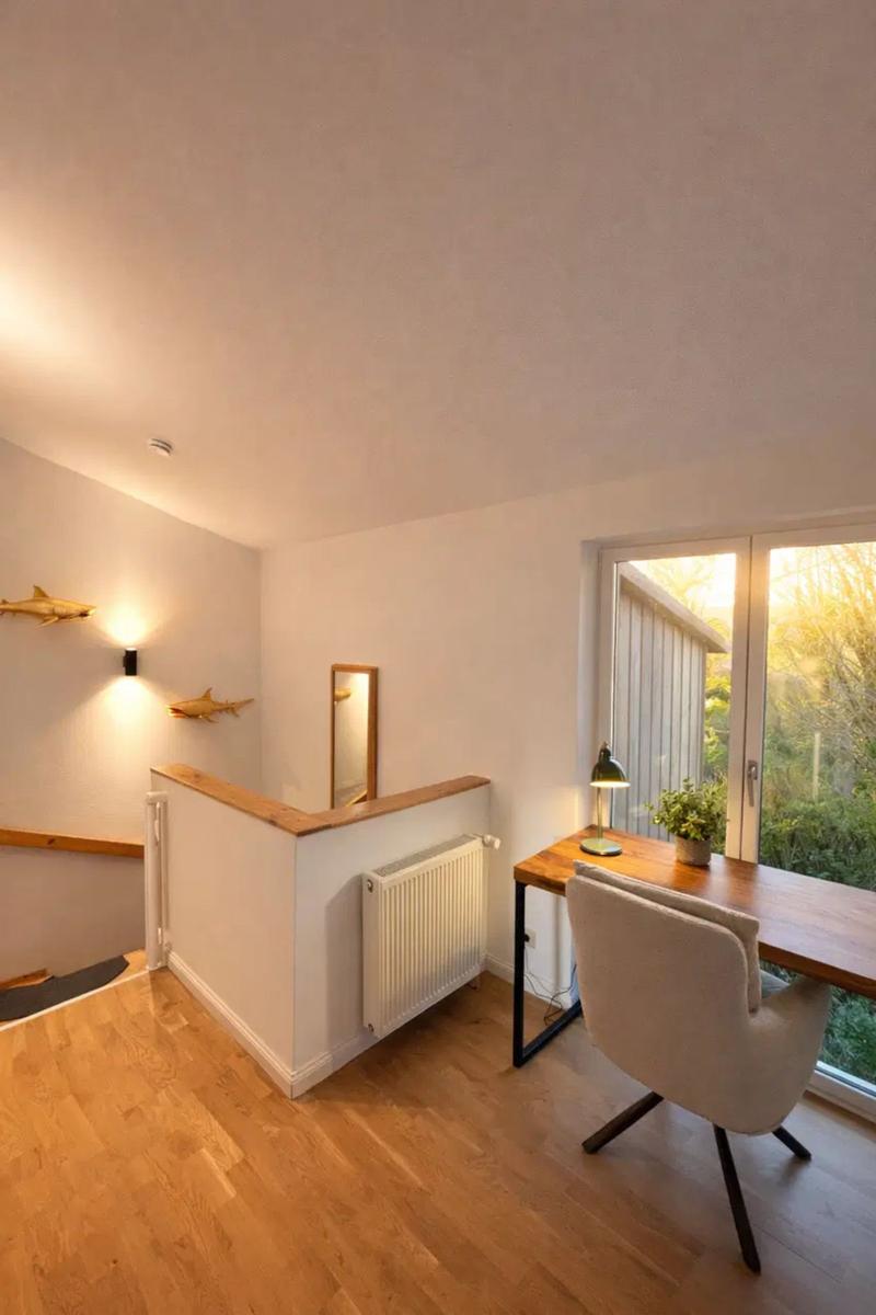 Arbeitszimmer mit Holztisch, Stuhl und Fenster. Wanddekoration und Heizung sind sichtbar.