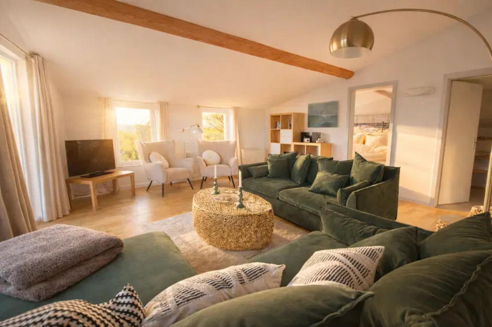 Wohnzimmer mit grünem Sofa, runden Tisch und Holzbalken an der Decke.