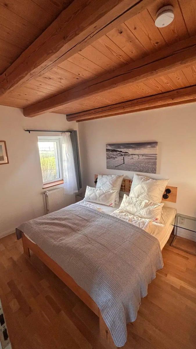 Schlafzimmer mit Holzboden, Bett und Fenster. Decke mit Holzbalken.