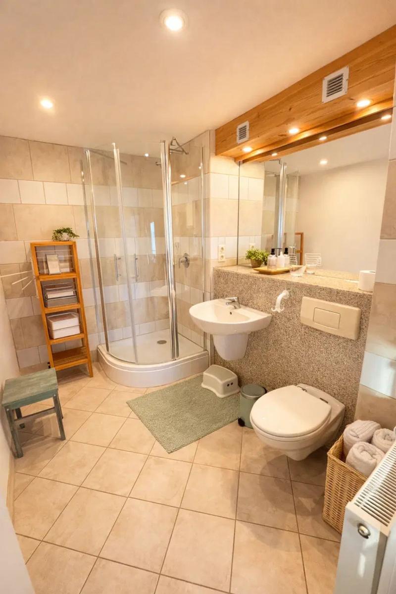 Badezimmer mit Dusche, Waschbecken und Toilette. Holzregal und geflochtener Korb.