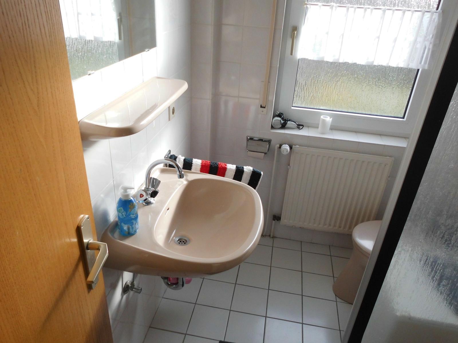 Bathroom with sink, toilet, and window with roller blind.