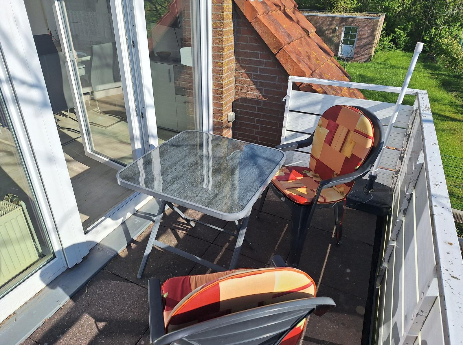 Terrace with table and two chairs, view of garden and house.