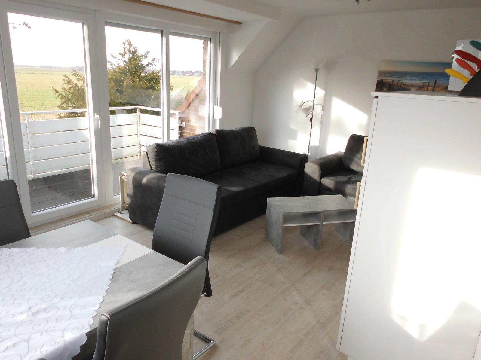 Living and dining area with sofa, table and chairs. Access to terrace with view of field.