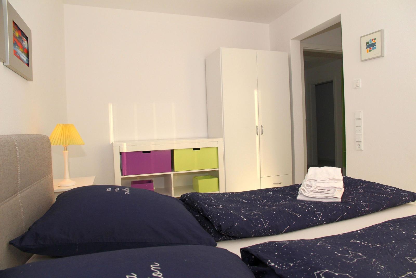 Schlafzimmer mit Doppelbett, Kleiderschrank und bunten Aufbewahrungskästen.
