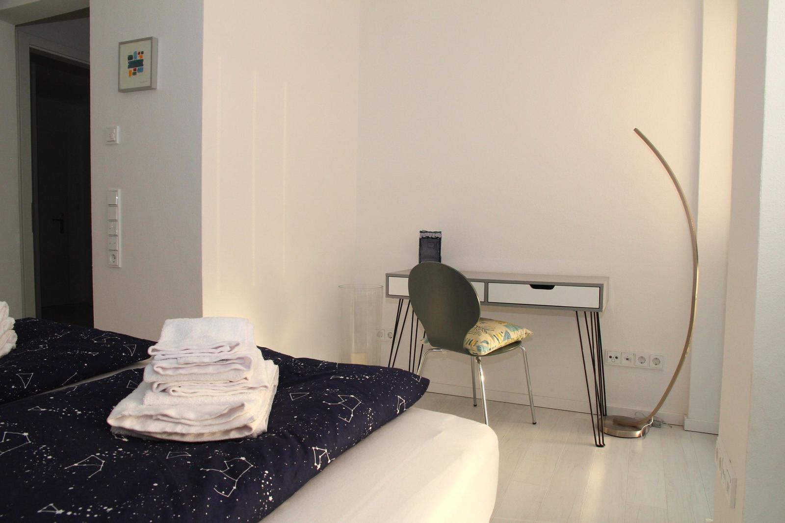 Schlafzimmer mit Bett, Schreibtisch und Stehlampe.