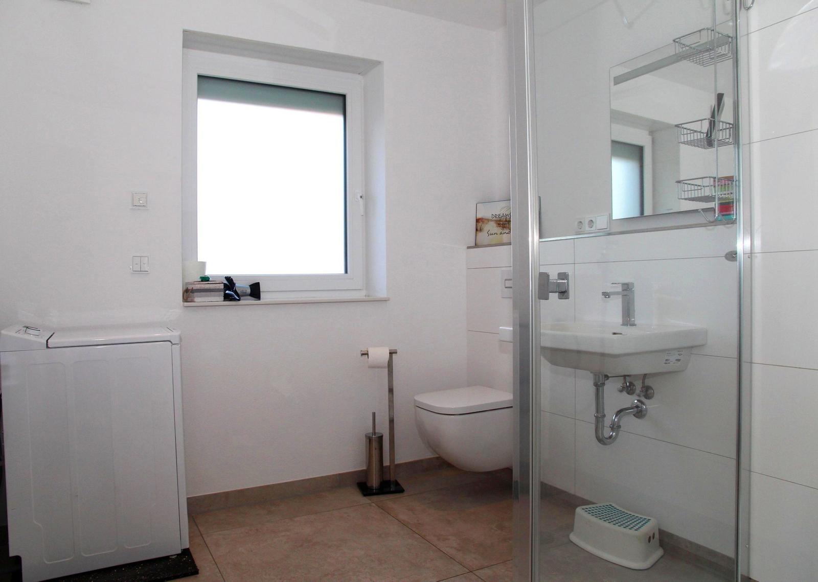 Badezimmer mit Waschmaschine, Toilette und Dusche.