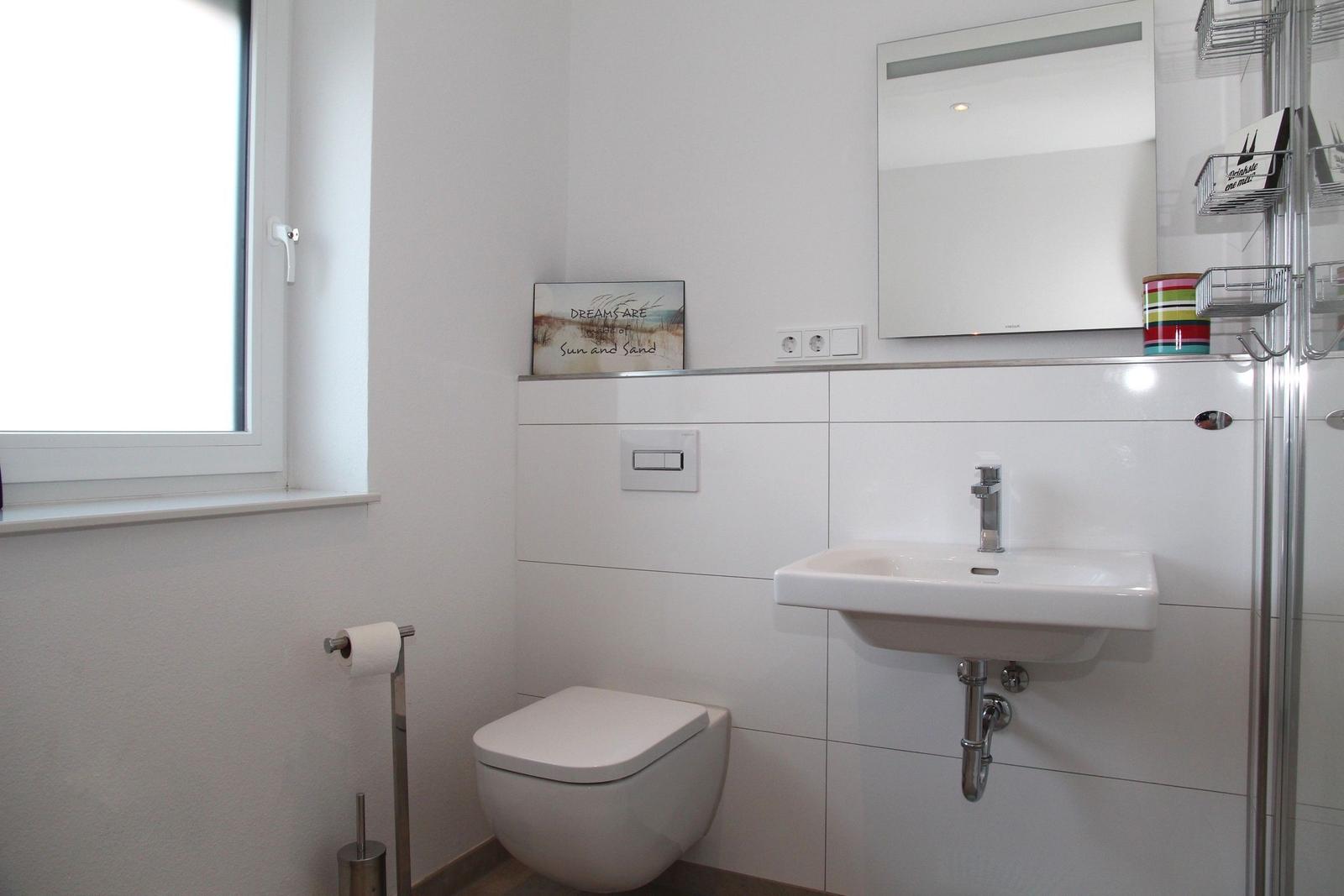 Badezimmer mit Toilette, Waschbecken und Spiegel. Fenster sorgt für Tageslicht.