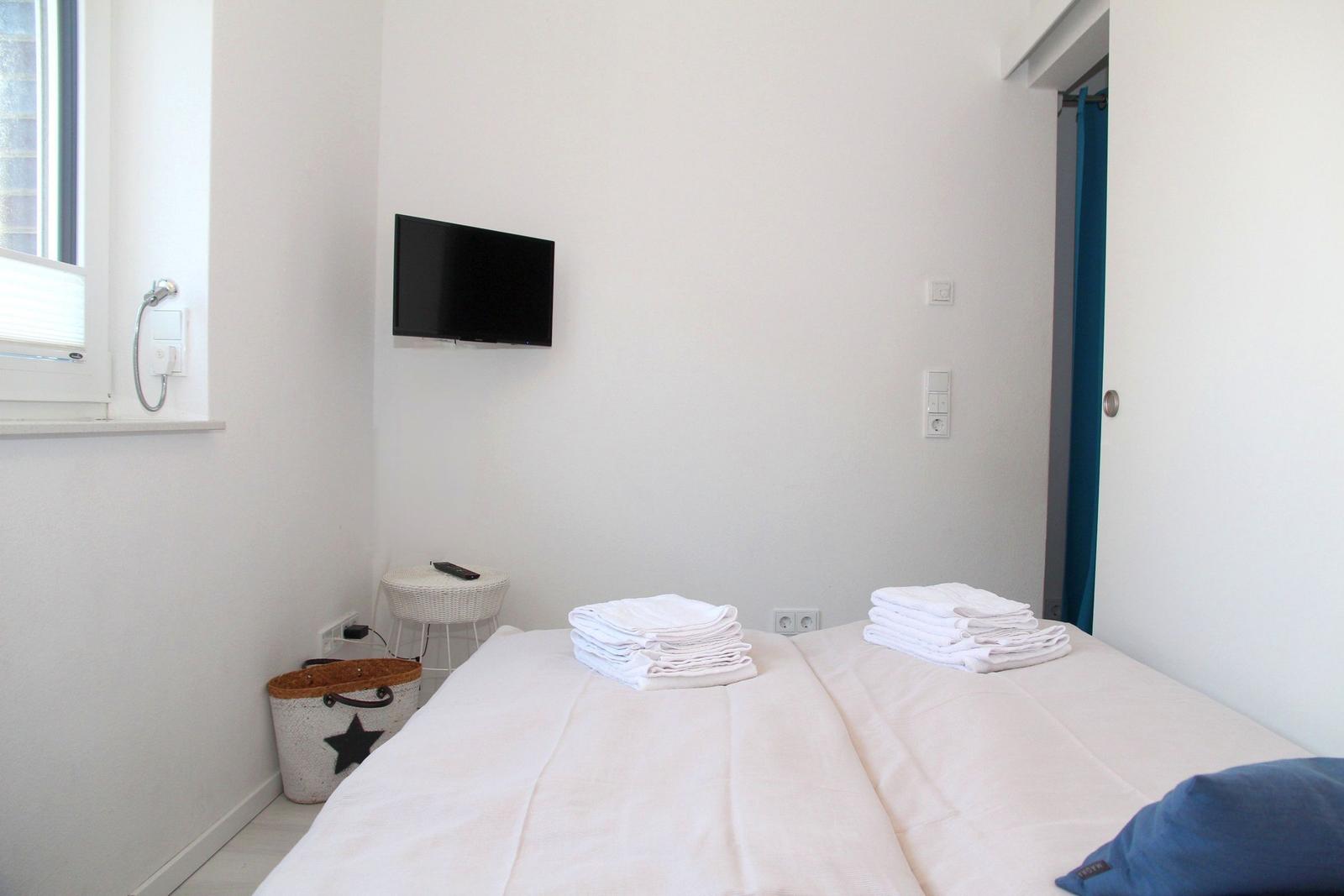 Zimmer mit Doppelbett, Fernseher und Fenster. Handtücher und Körbchen sind vorhanden.