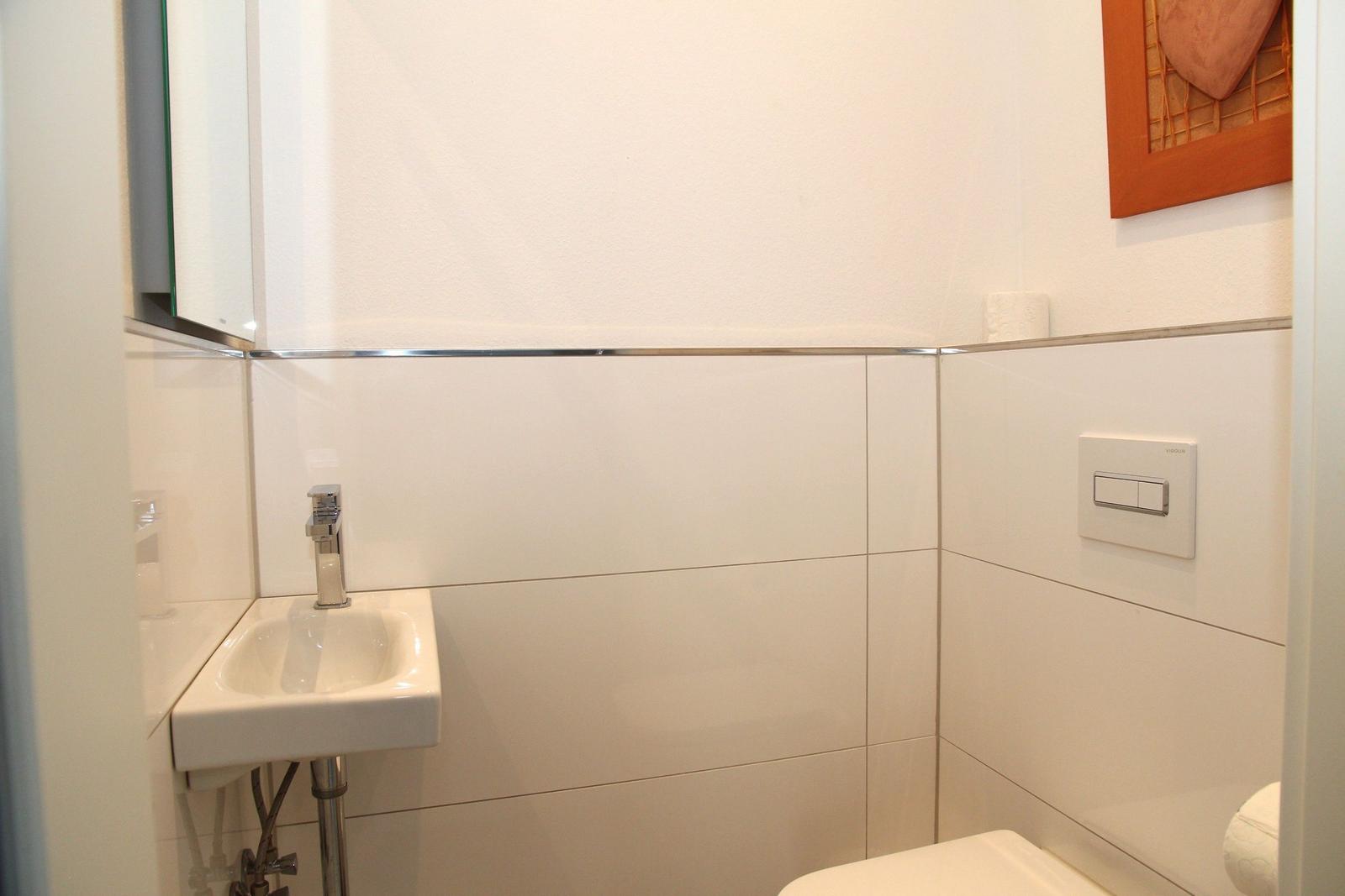 Badezimmer mit Waschbecken, Spiegel und Toilette. Weiße Fliesen und moderne Armaturen.