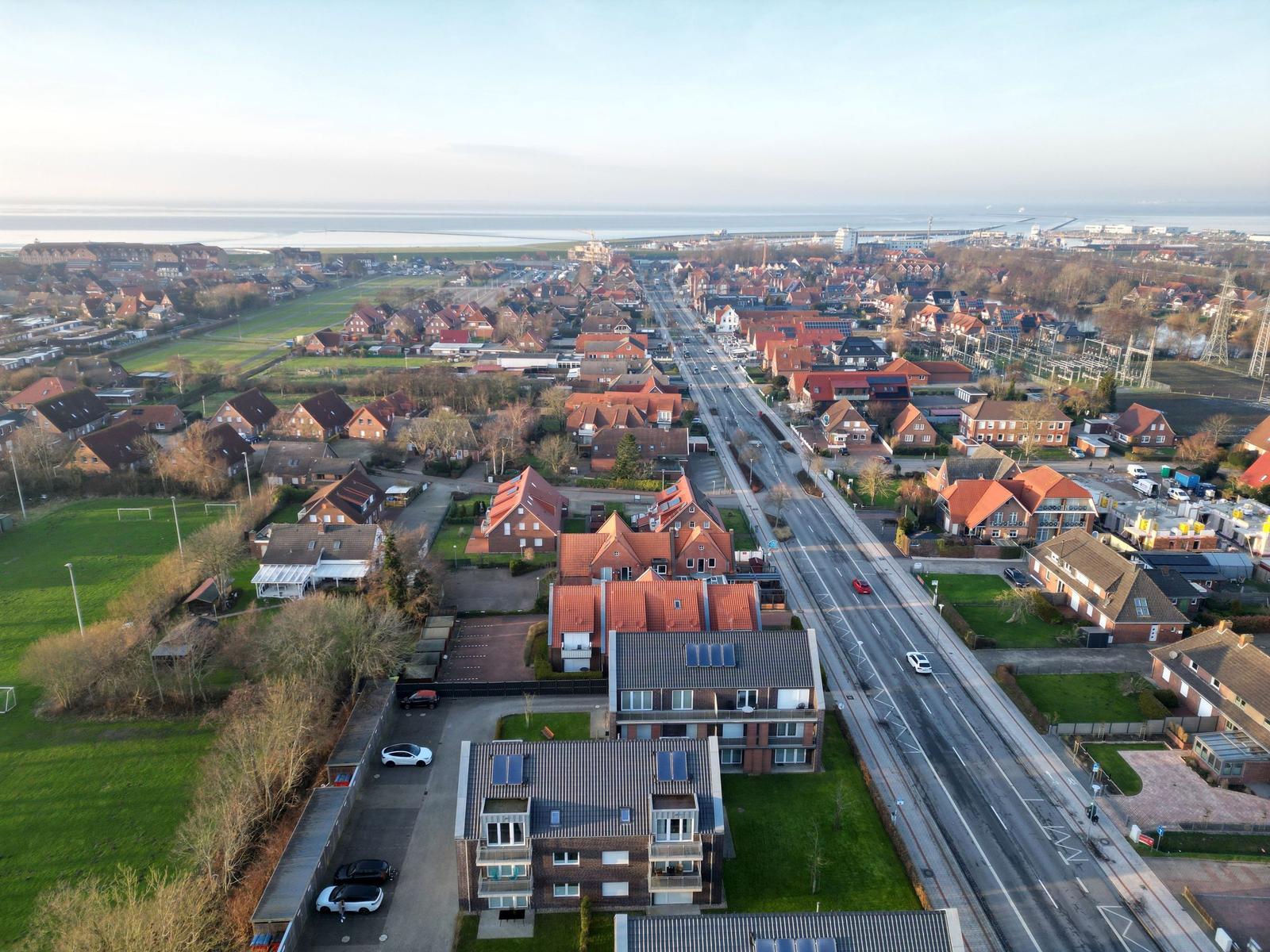 Aerial view of residential area with red-roofed houses and coastal landscape.