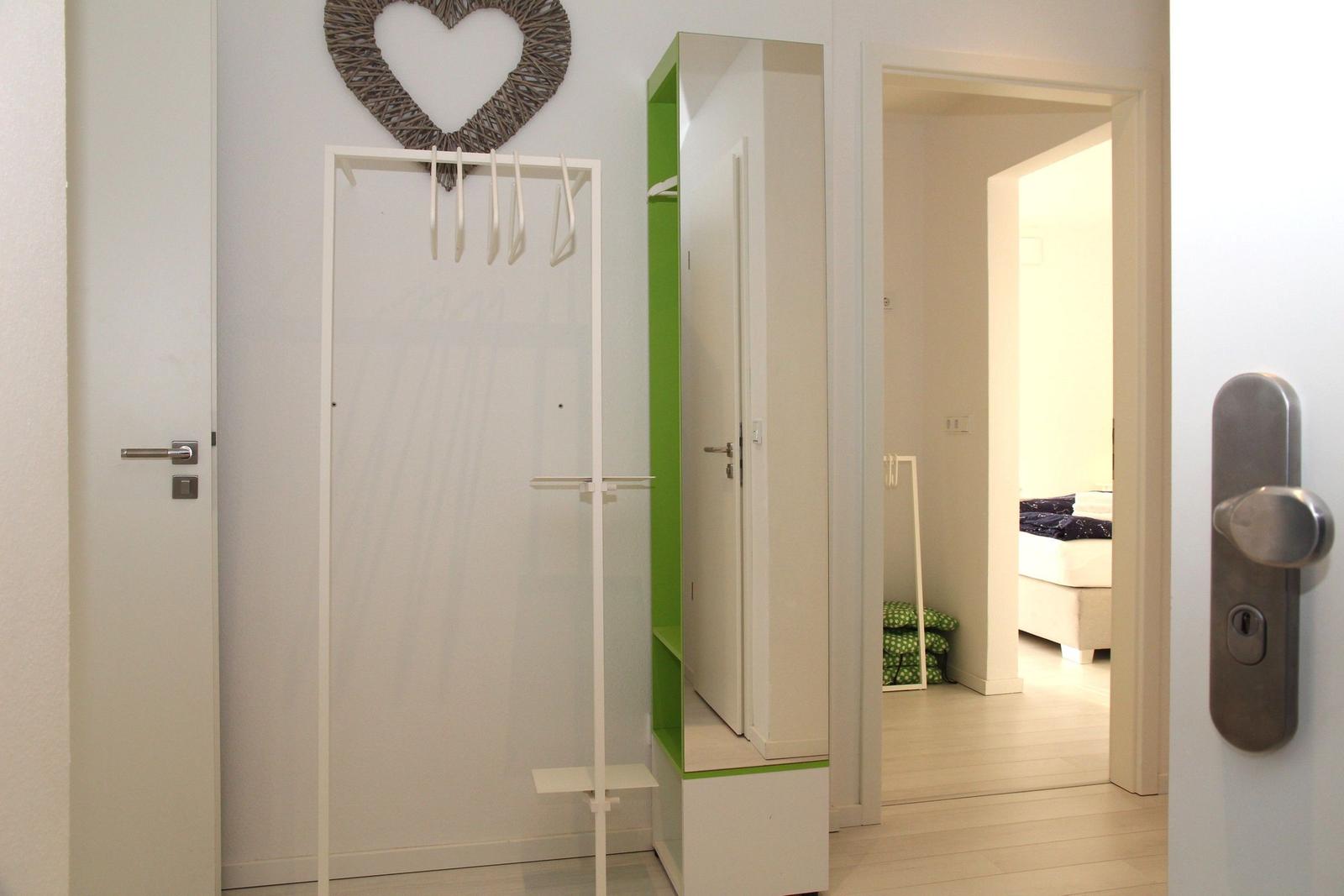 Eingangsbereich mit Kleiderständer und grünem Schrank. Durchgang zu Schlafzimmer mit Bett.