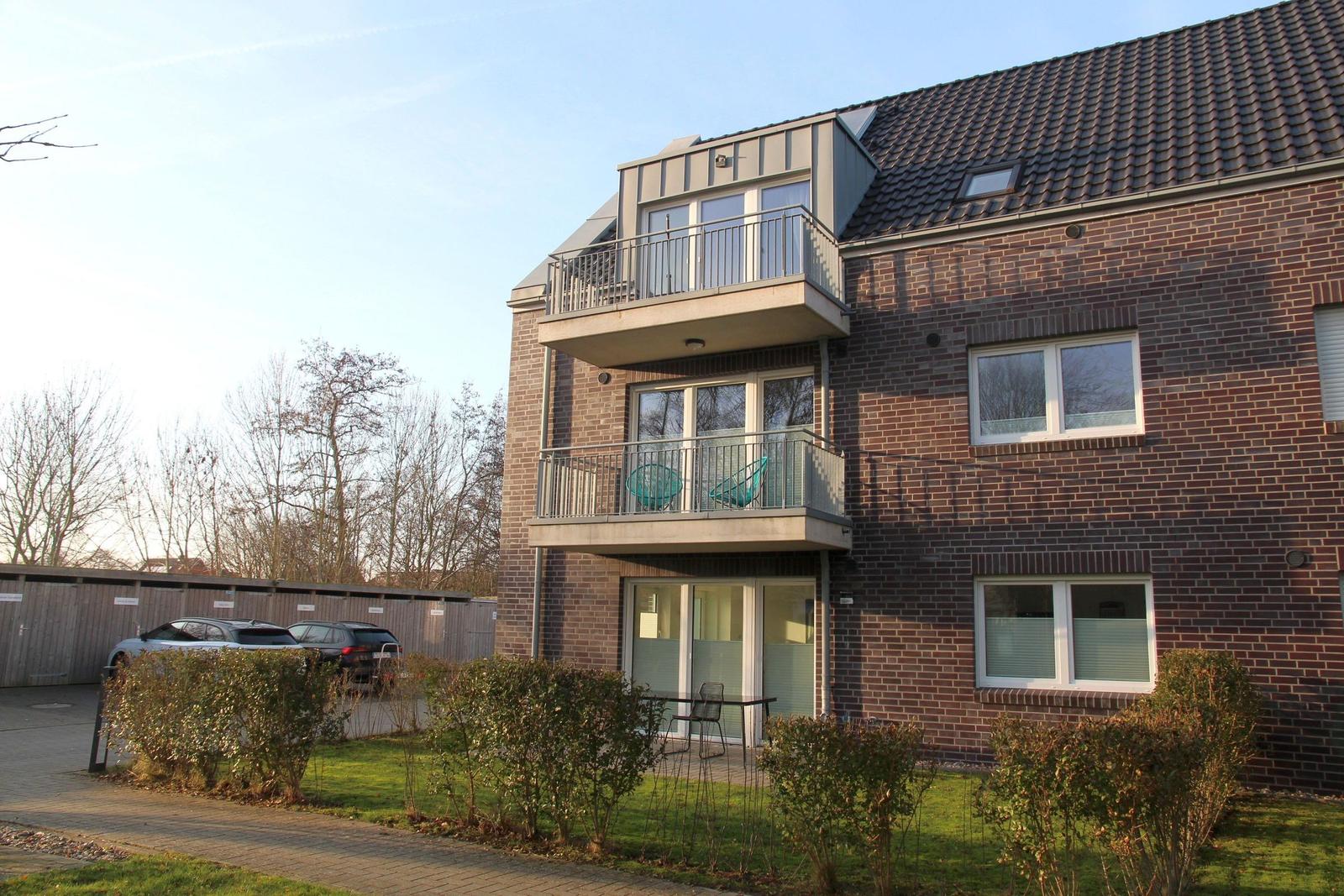 Zweistöckiges Haus mit Balkonen und Garten. Zwei Balkone mit Stühlen. Parkplatz vorne.