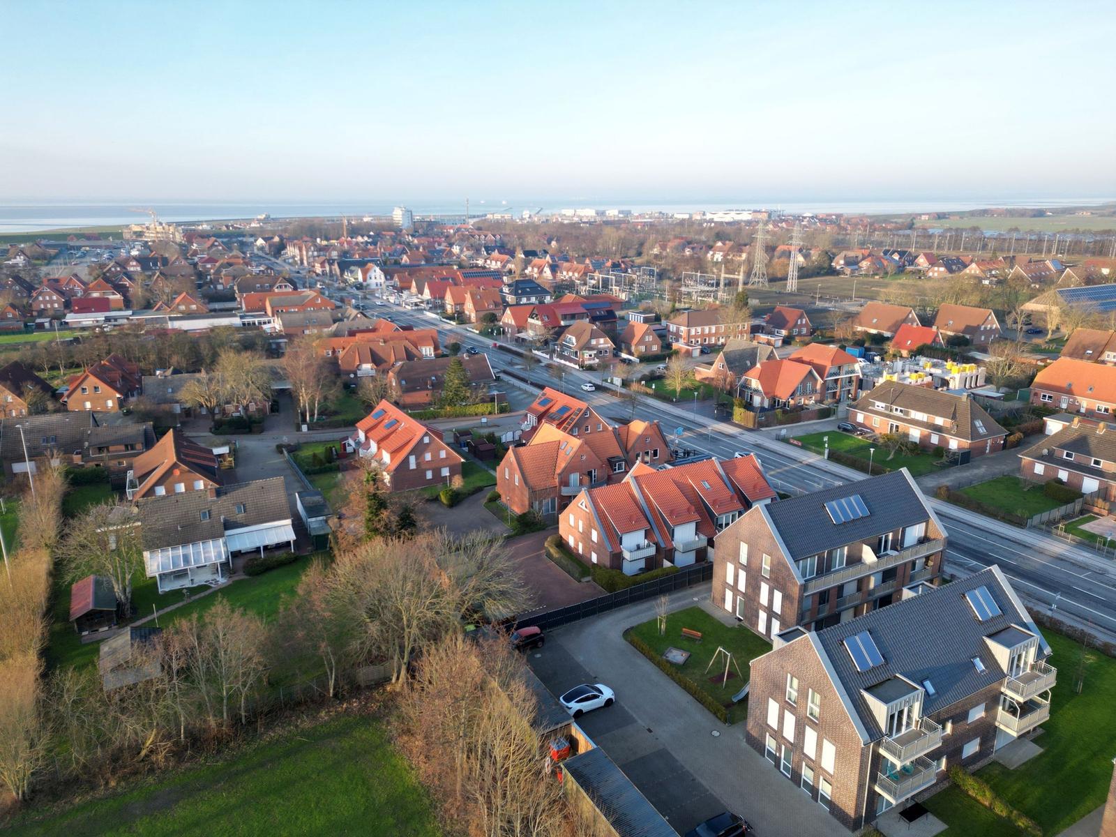 Aerial view of residential area with red-roofed houses and sea in distance.