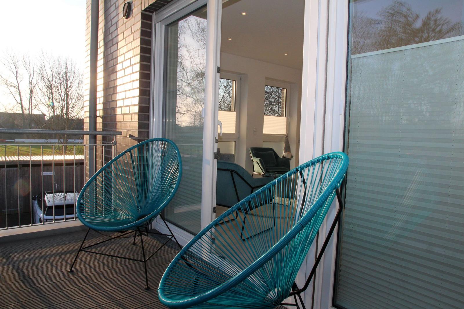 Terrasse mit zwei türkisfarbenen Sesseln und Blick in das Wohnzimmer.