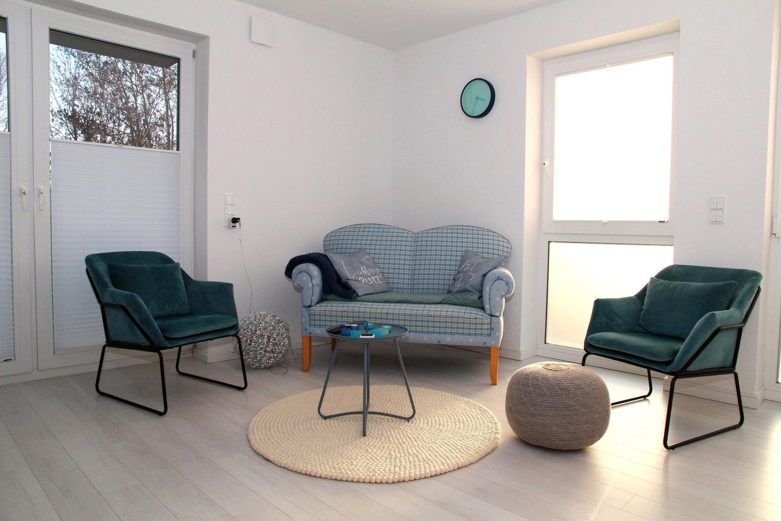 Wohnzimmer mit Sofa und zwei Sesseln, runden Teppich und Tisch.