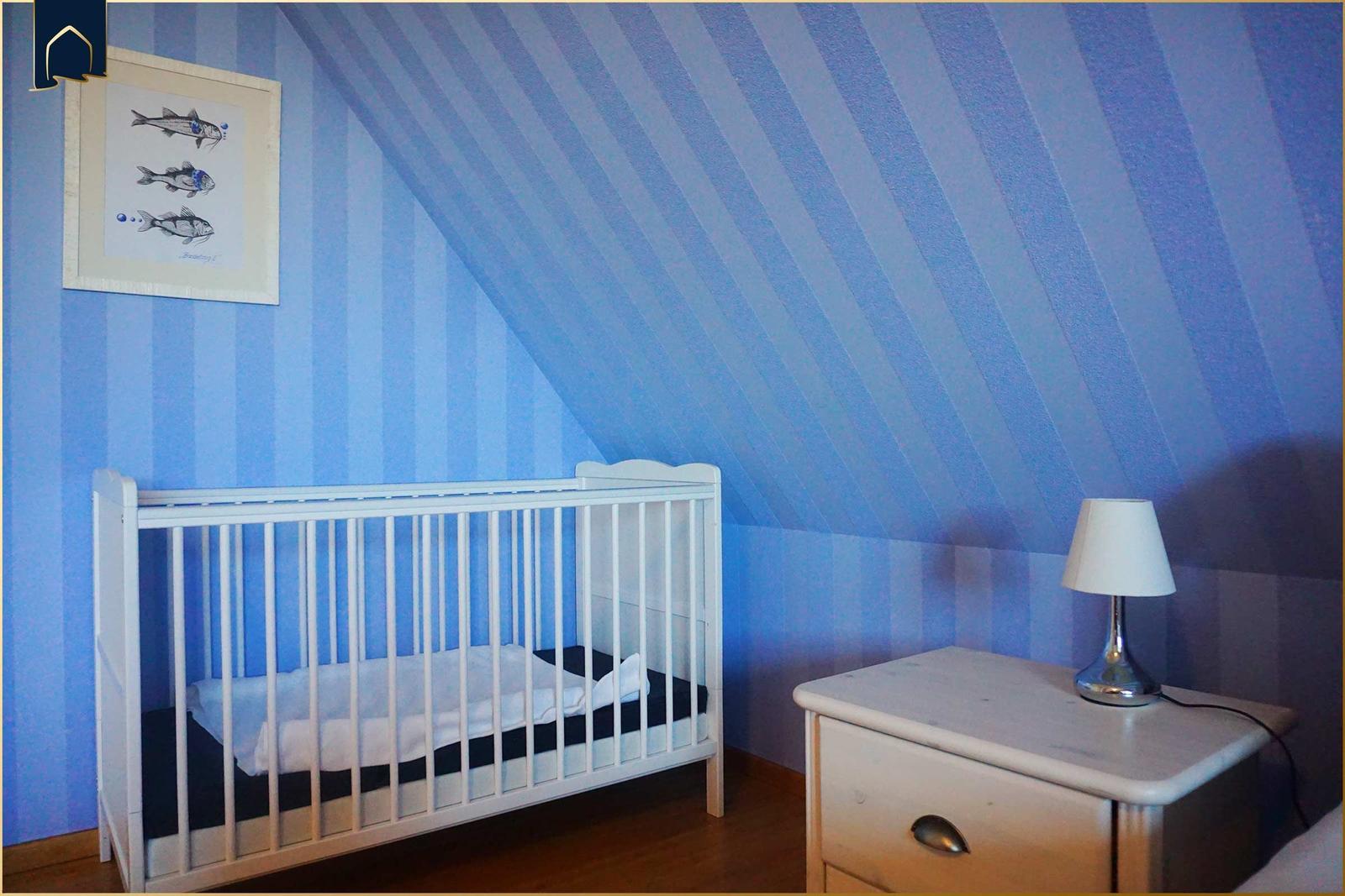 Kinderzimmer mit Kinderbett, Nachttisch und Wandbild an blau gestreifter Wand.