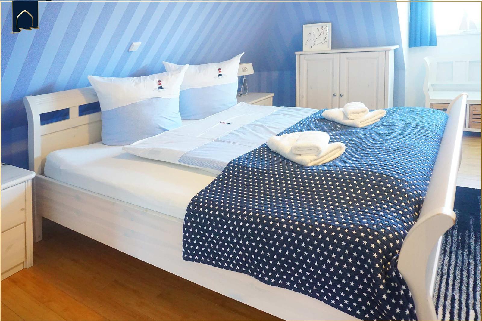 Schlafzimmer mit Bett, Kissen und blauer Wandtapete mit Streifen.