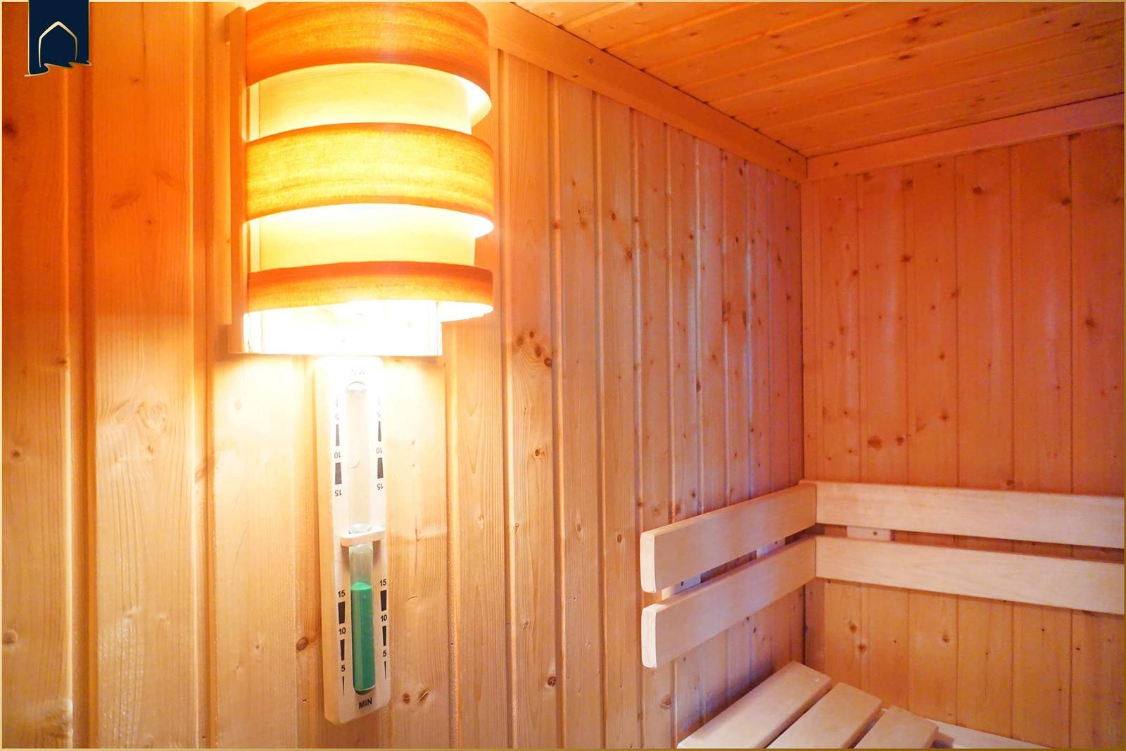 Sauna mit Holzwand und Sitzbank. An der Wand hängt eine Lampe und ein Timer.