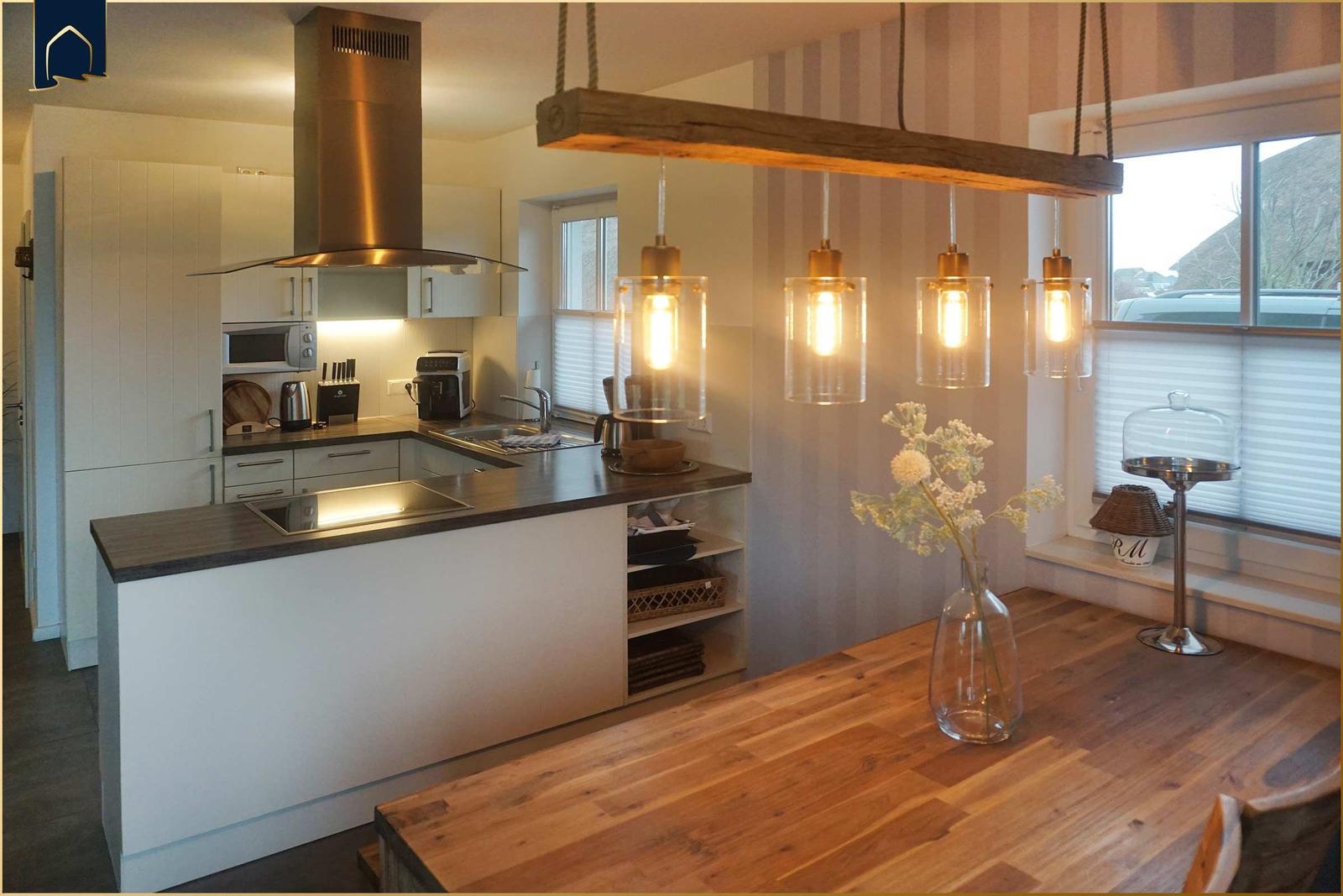 Küche mit Holztablett und hängenden Lampen. Fenster mit Jalousien und Blumen in Glasvase.