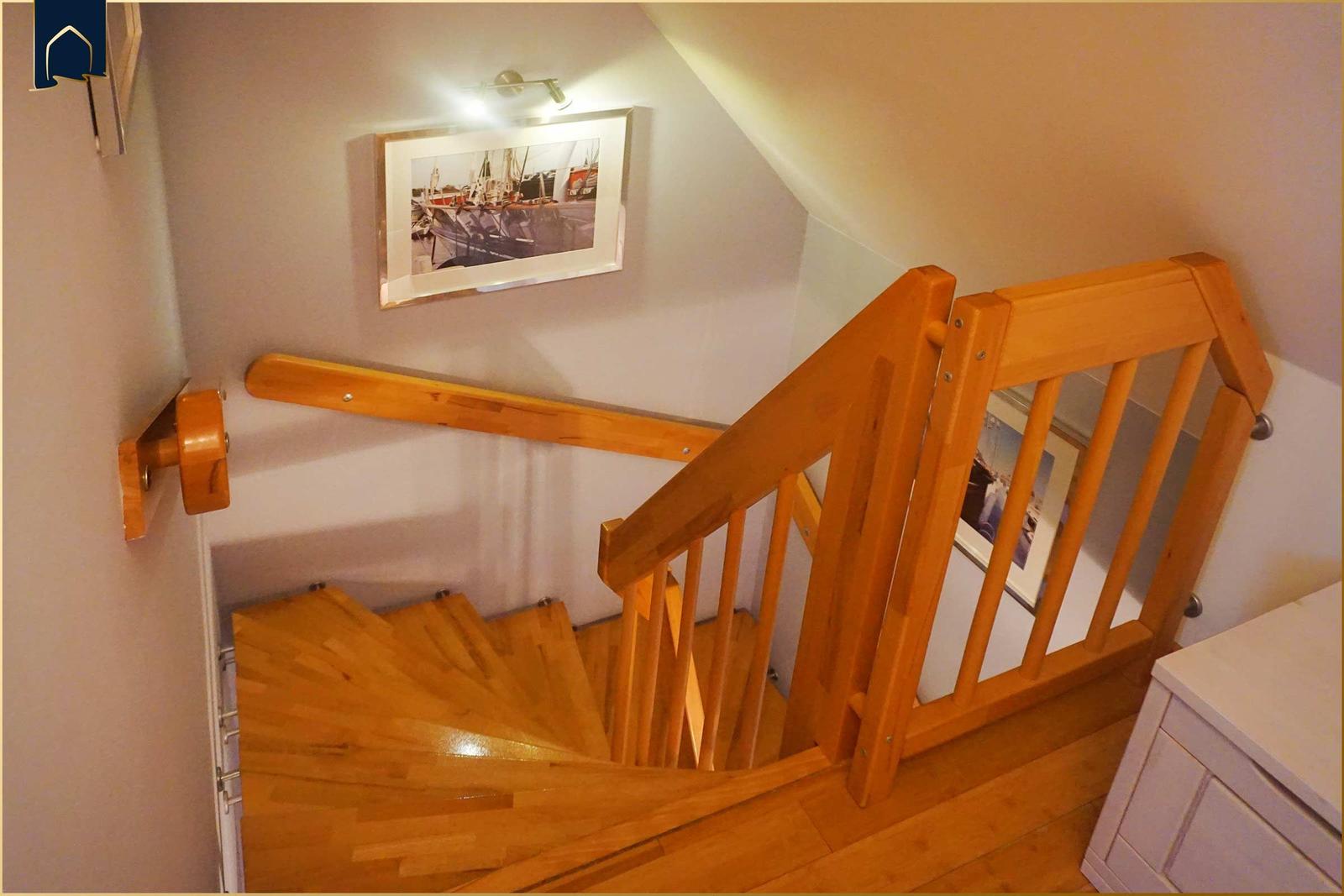 Holzgetreppe mit Geländer führt nach oben. Wandbild zeigt Schiffe. Raum mit hellem Holzboden.