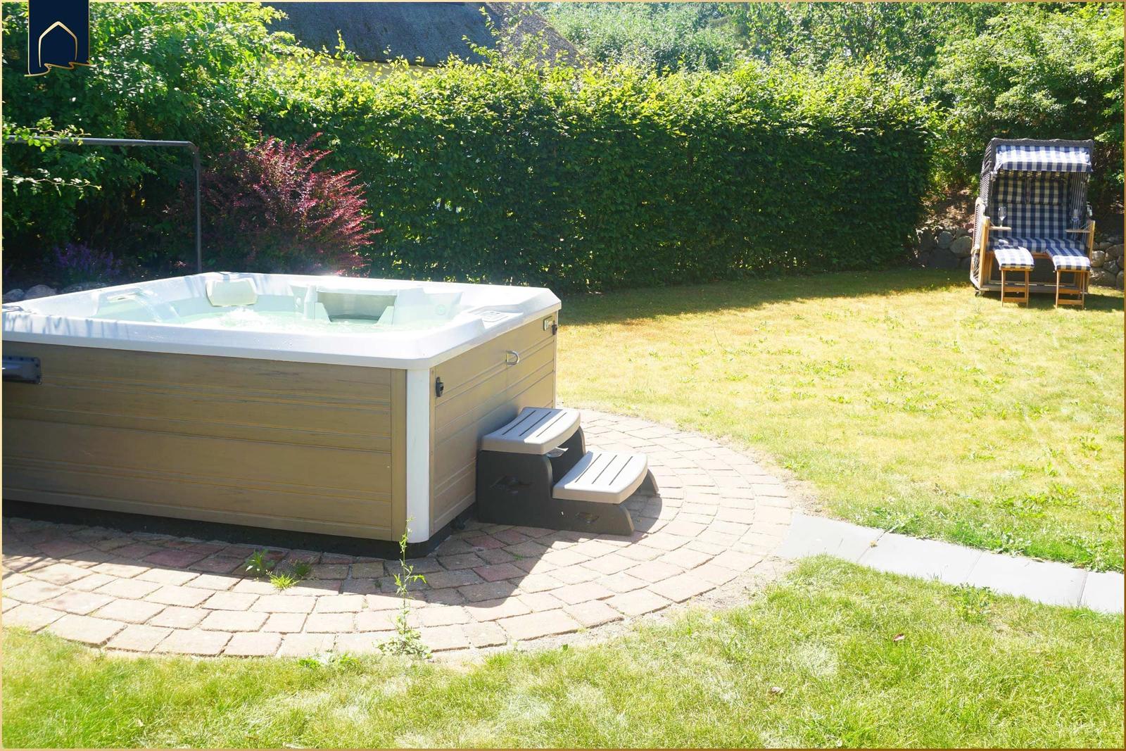 Whirlpool auf Terrasse mit Garten und Liegestuhl im Hintergrund.