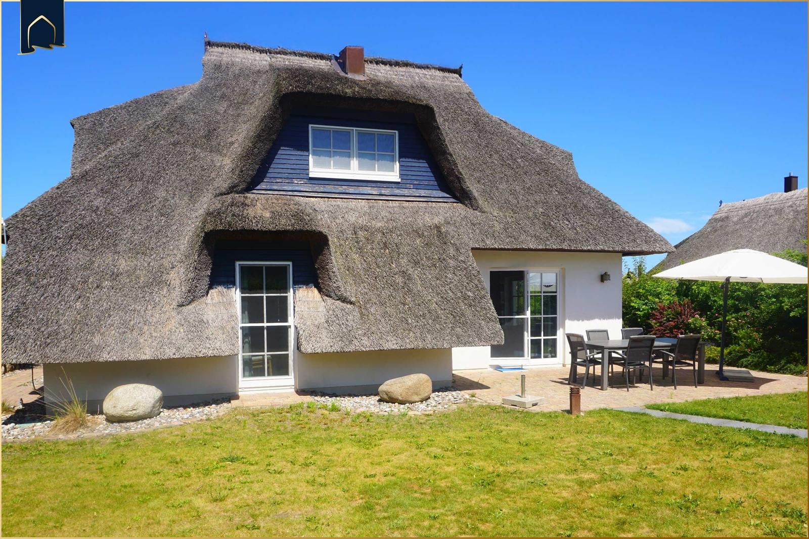 Dorfhaus mit Strohdach, Terrasse und Garten. Weiße Wände und Holzelemente.