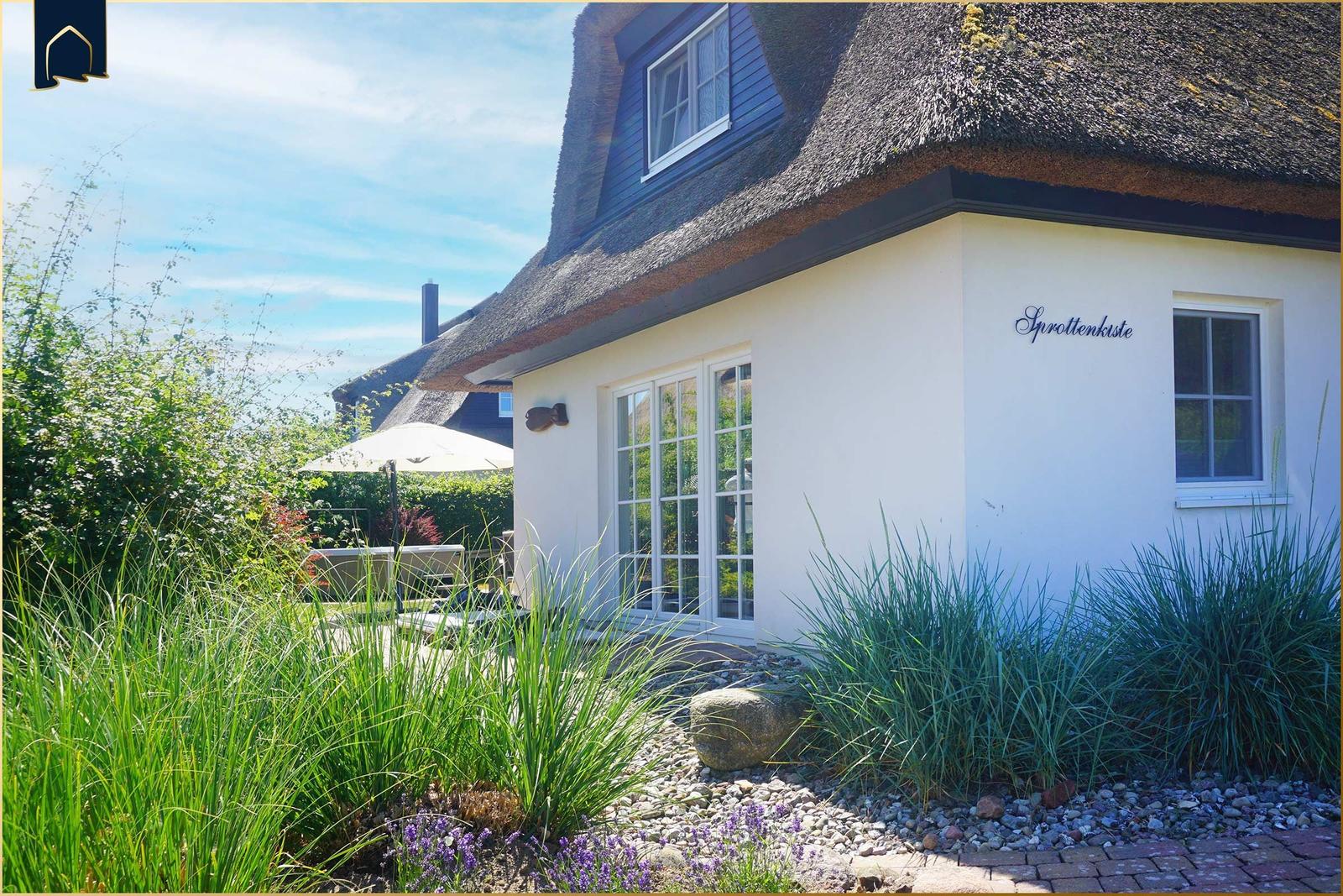 Haus mit Strohdach, weißer Fassade und Gartenbereich mit Sitzgelegenheit.