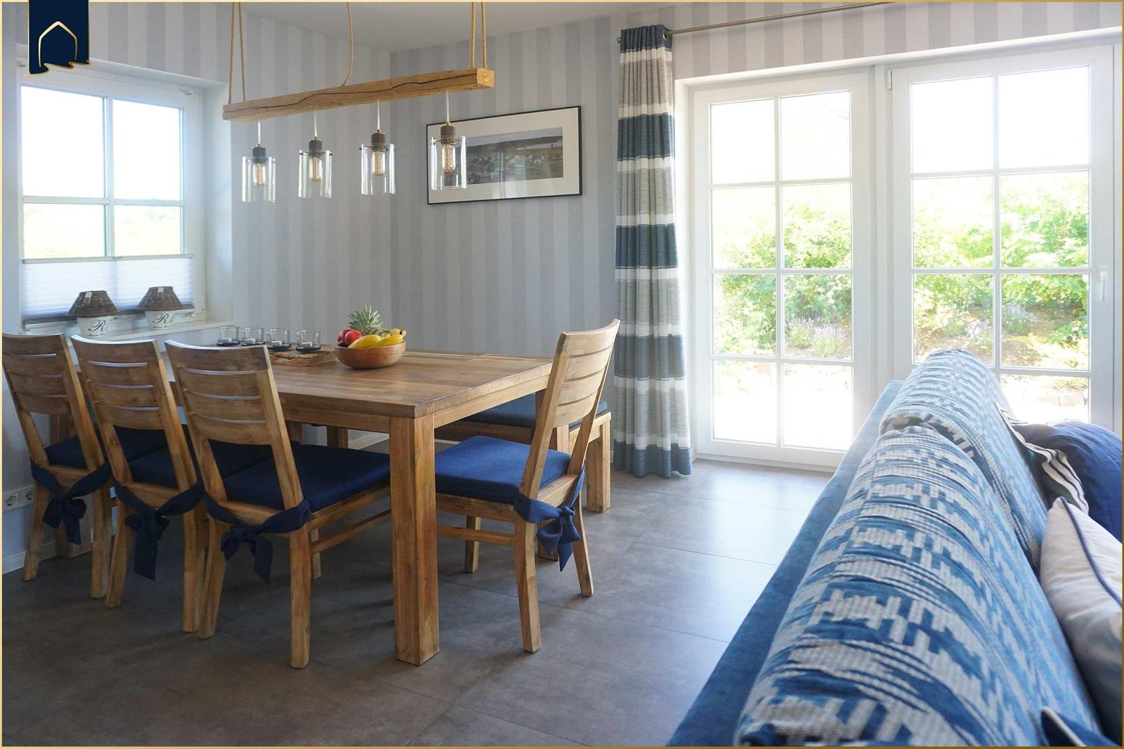 Essbereich mit Holztisch und Stühlen, Sofa und Fenster zur Terrasse.