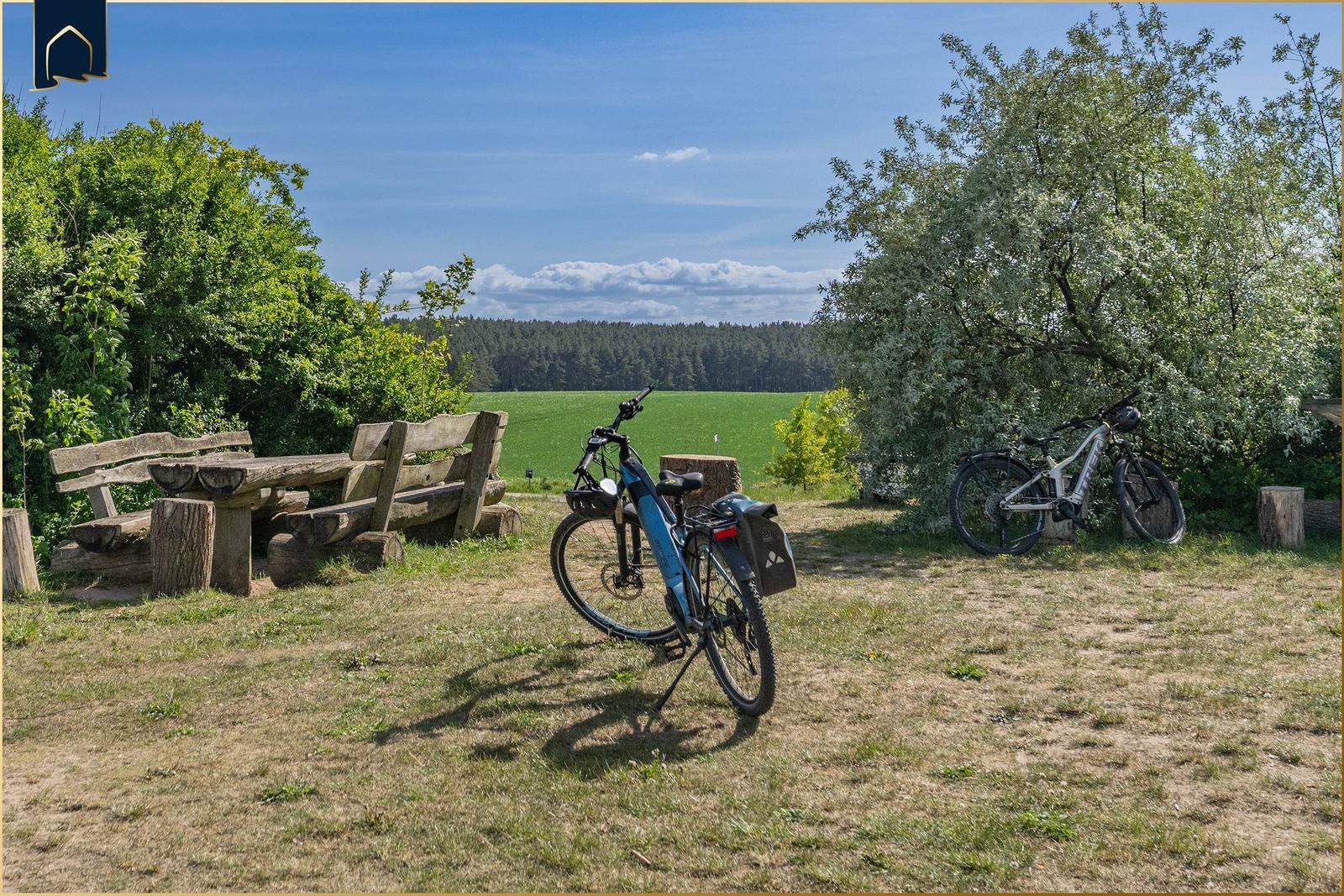 Zwei Fahrräder stehen im Freien neben einer Holzbank und einem grünen Feld.