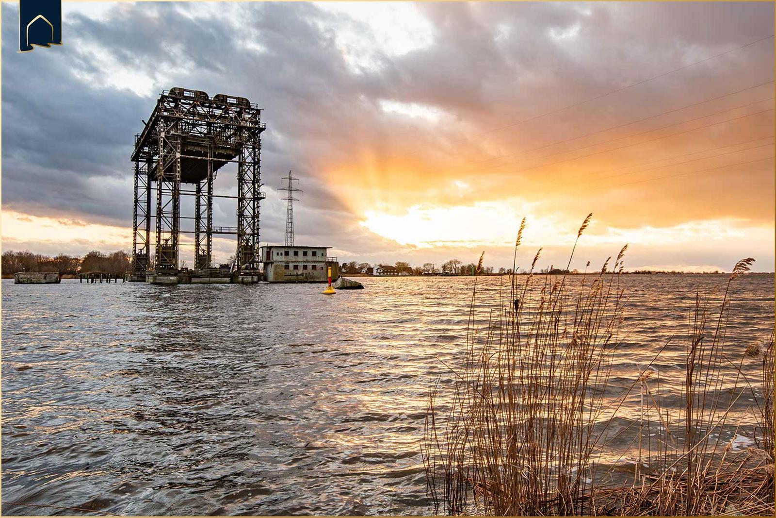 Wasserfläche mit Industrieanlage und Sonnenuntergang.