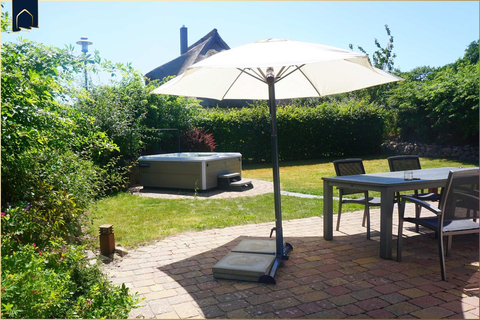 Terrasse mit Tisch, Stühlen und Sonnenschirm. Hintergrund: Whirlpool und grüner Garten.