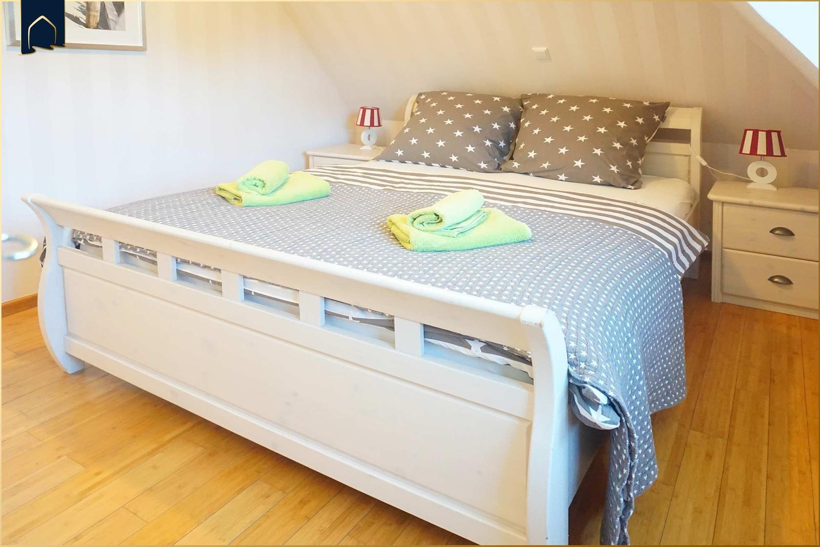 Schlafzimmer mit weißem Bett, Holzboden und zwei Nachttischen mit Lampen.