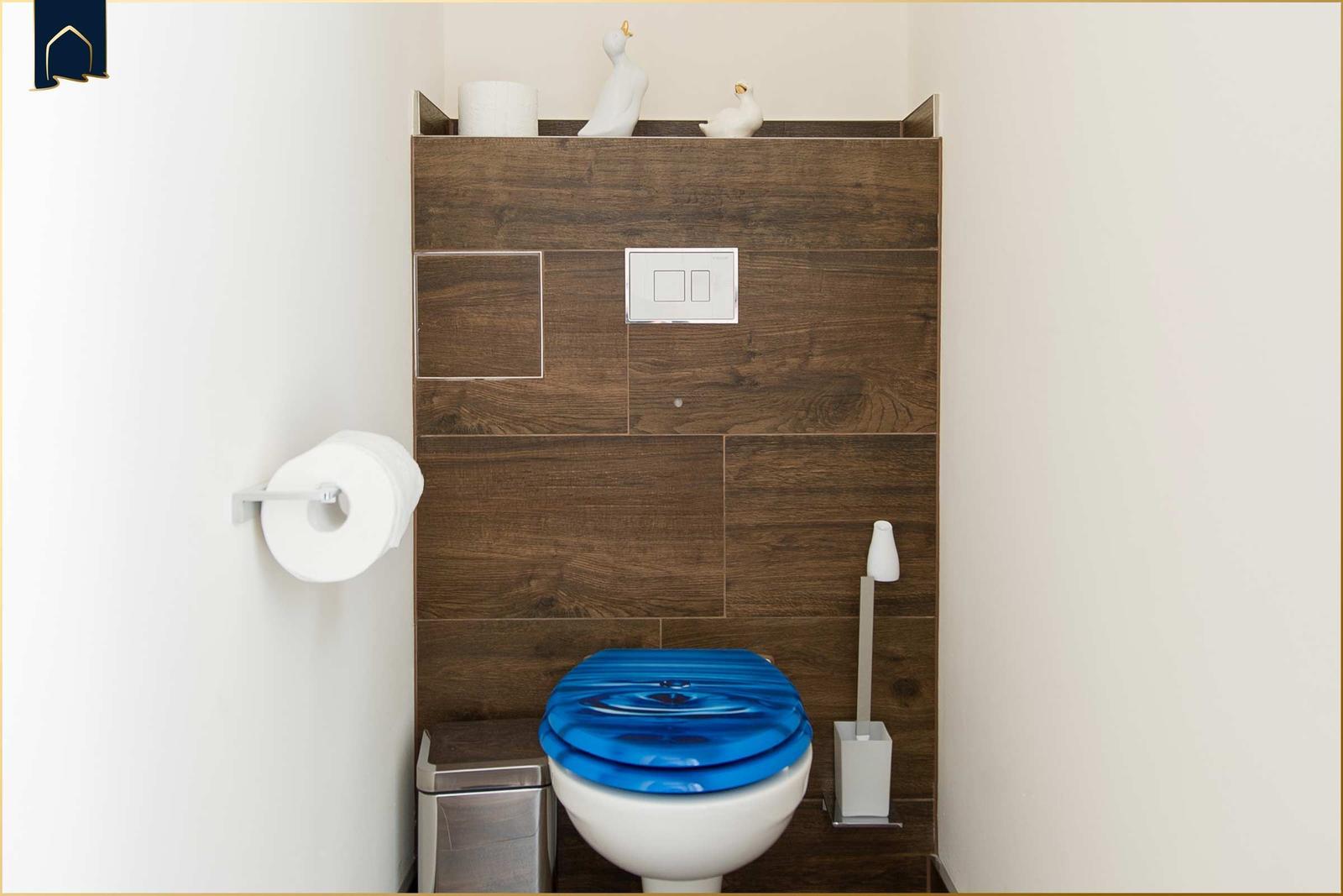 Toilette mit blauem Sitz, Holzwand und Toilettenpapierhalter.