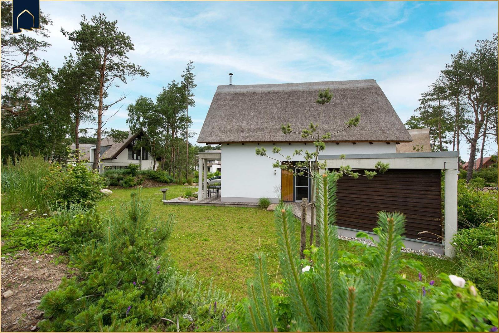 Moderne Villa mit Strohdach und Holzgarage in grüner Umgebung.