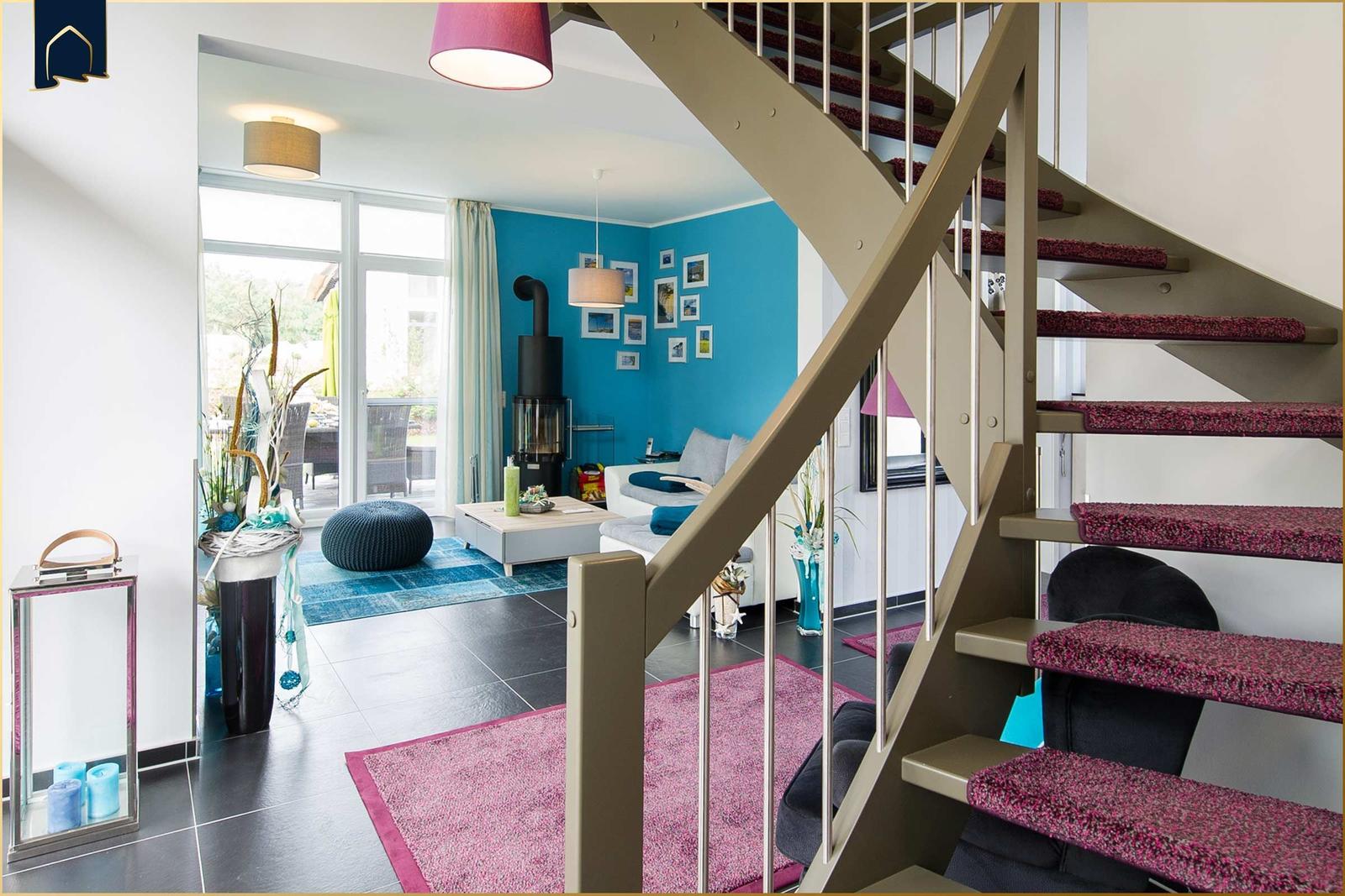 Eingangsbereich mit Treppe und Blick in Wohnzimmer mit blauer Wand und Kamin.