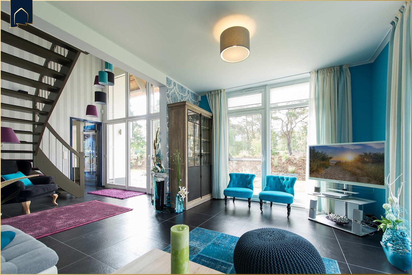 Wohnzimmer mit blauen Sesseln, großen Fenstern und schwarzem Boden