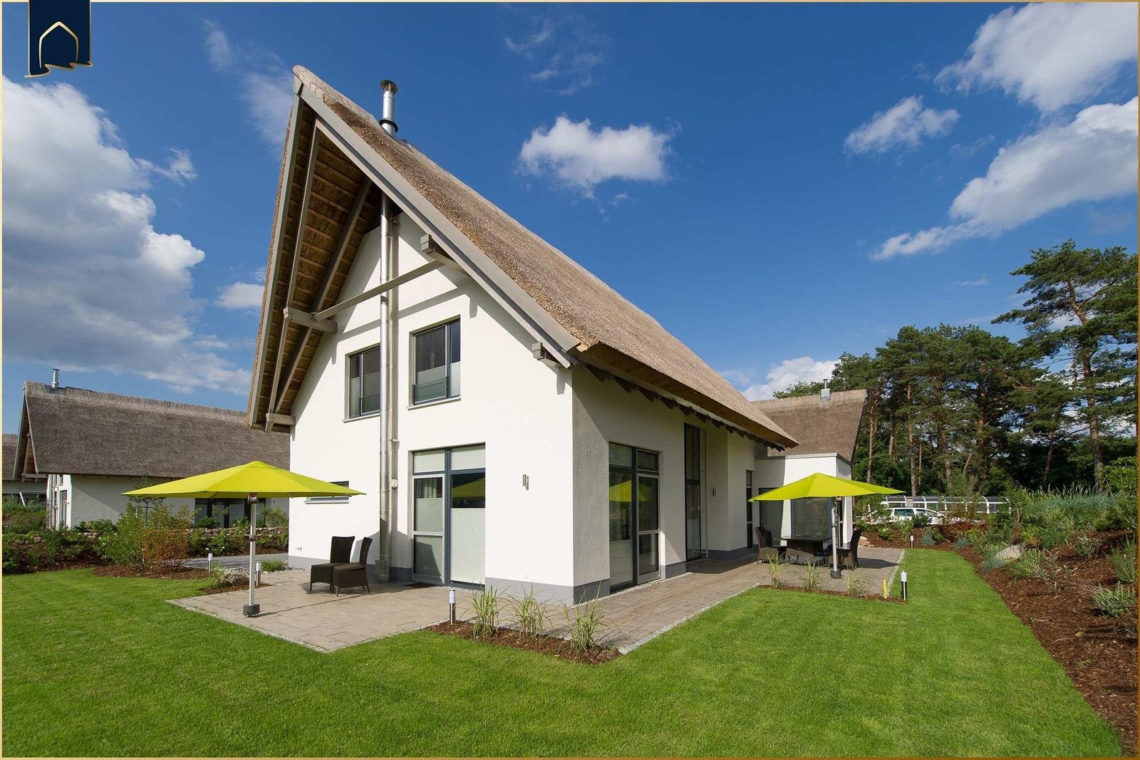 Moderne Villa mit Strohdach, Terrasse und grünem Garten unter blauem Himmel.