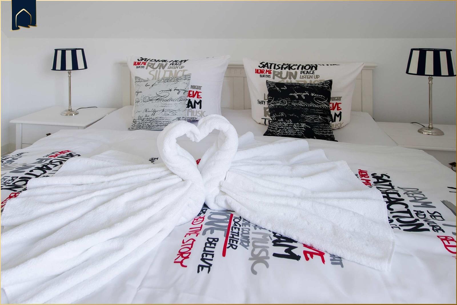 Doppelbett mit weißen Kissen und Handtüchern in Herzform.