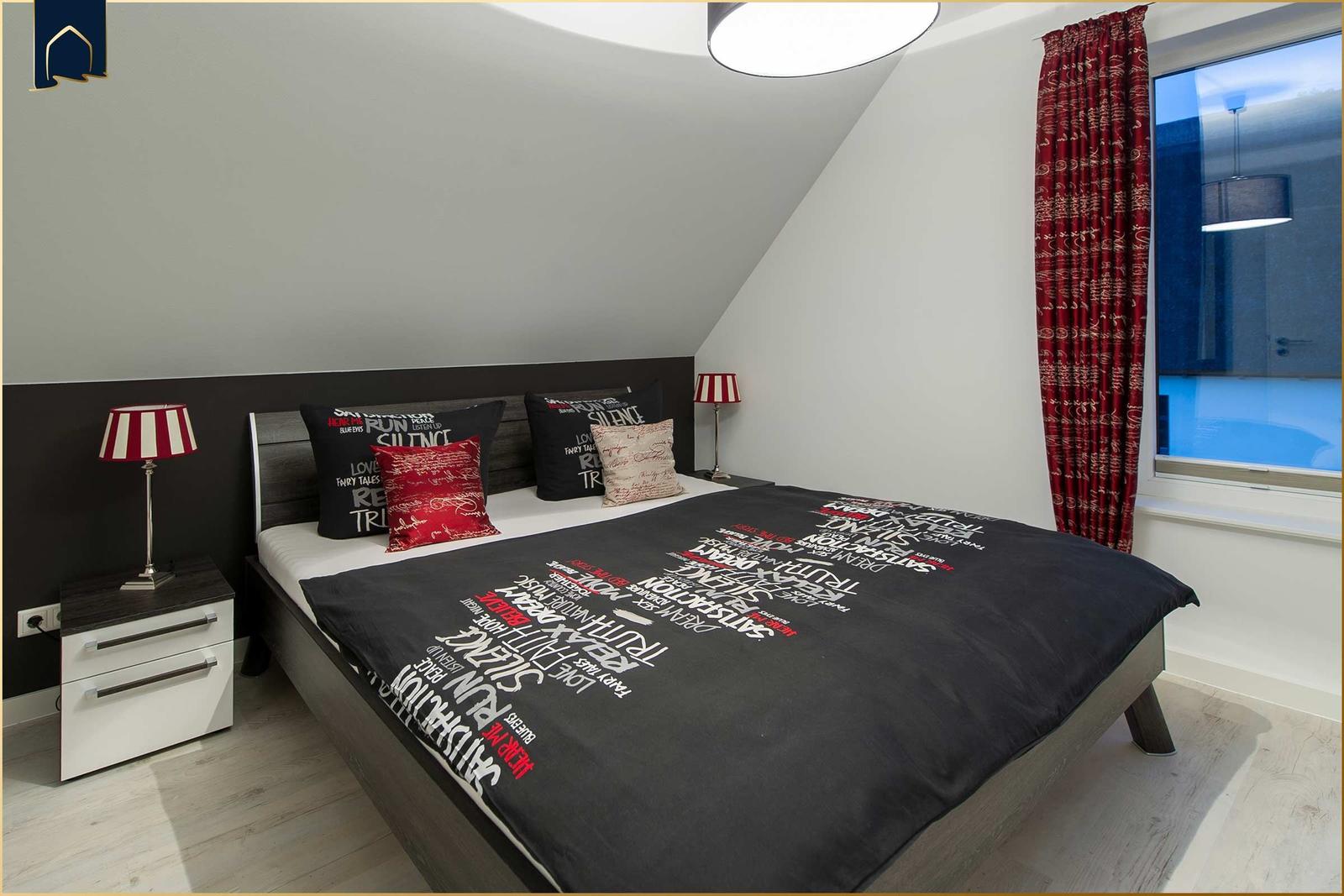 Schlafzimmer mit Dachschrägen, Bett mit Kissen und Vorhängen.